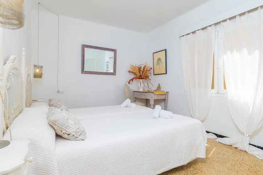 A bright bedroom with a large white bed and sheer curtains by the window.