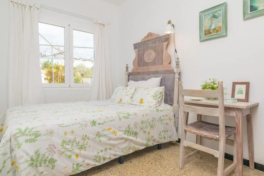 A bright bedroom with a floral bedspread, a desk, and a window.