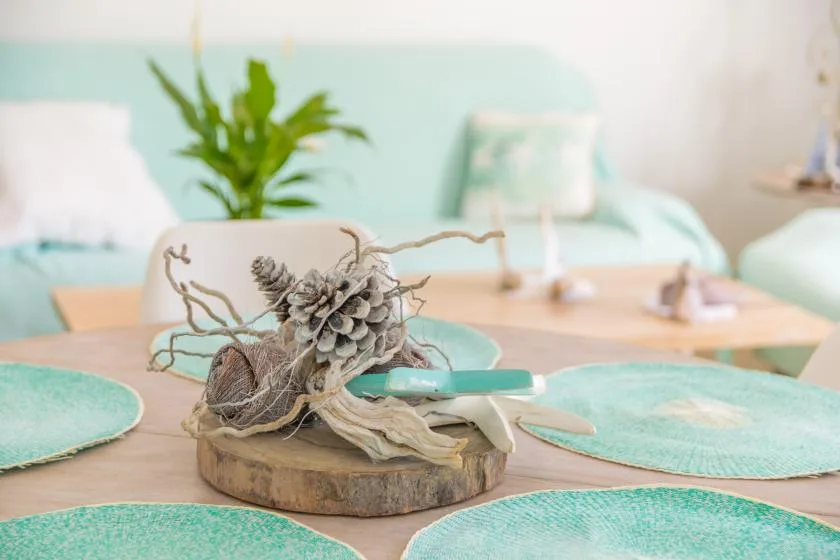 A dining table has turquoise placemats and a pinecone centerpiece.