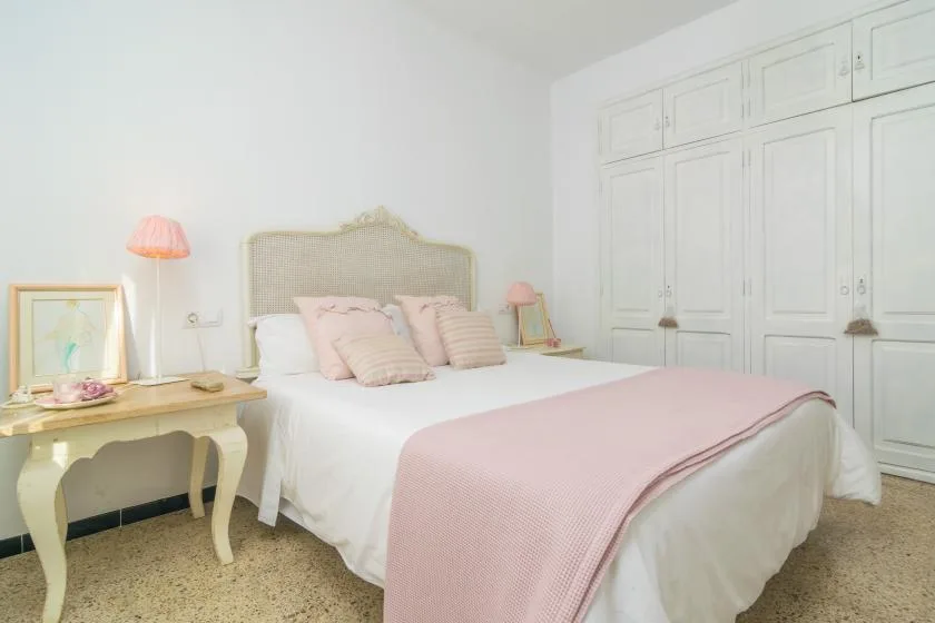 A bedroom with a bed dressed in white and pink bedding.