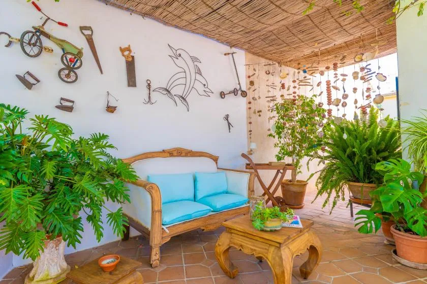A plant-filled patio seating area features a blue-cushioned bench and a wooden coffee table.