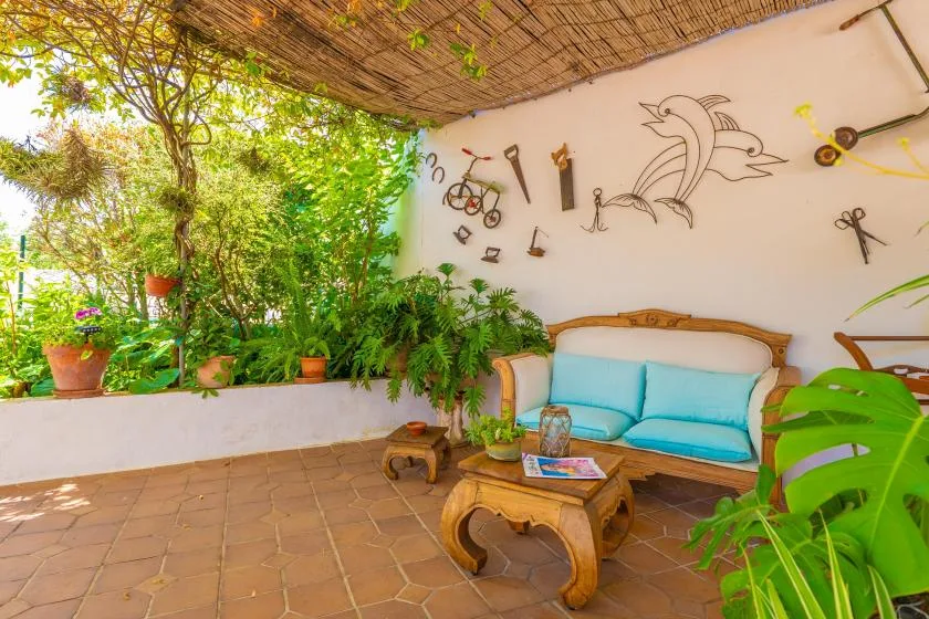 A covered patio seating area with turquoise cushions, plants, and decorative wall art.