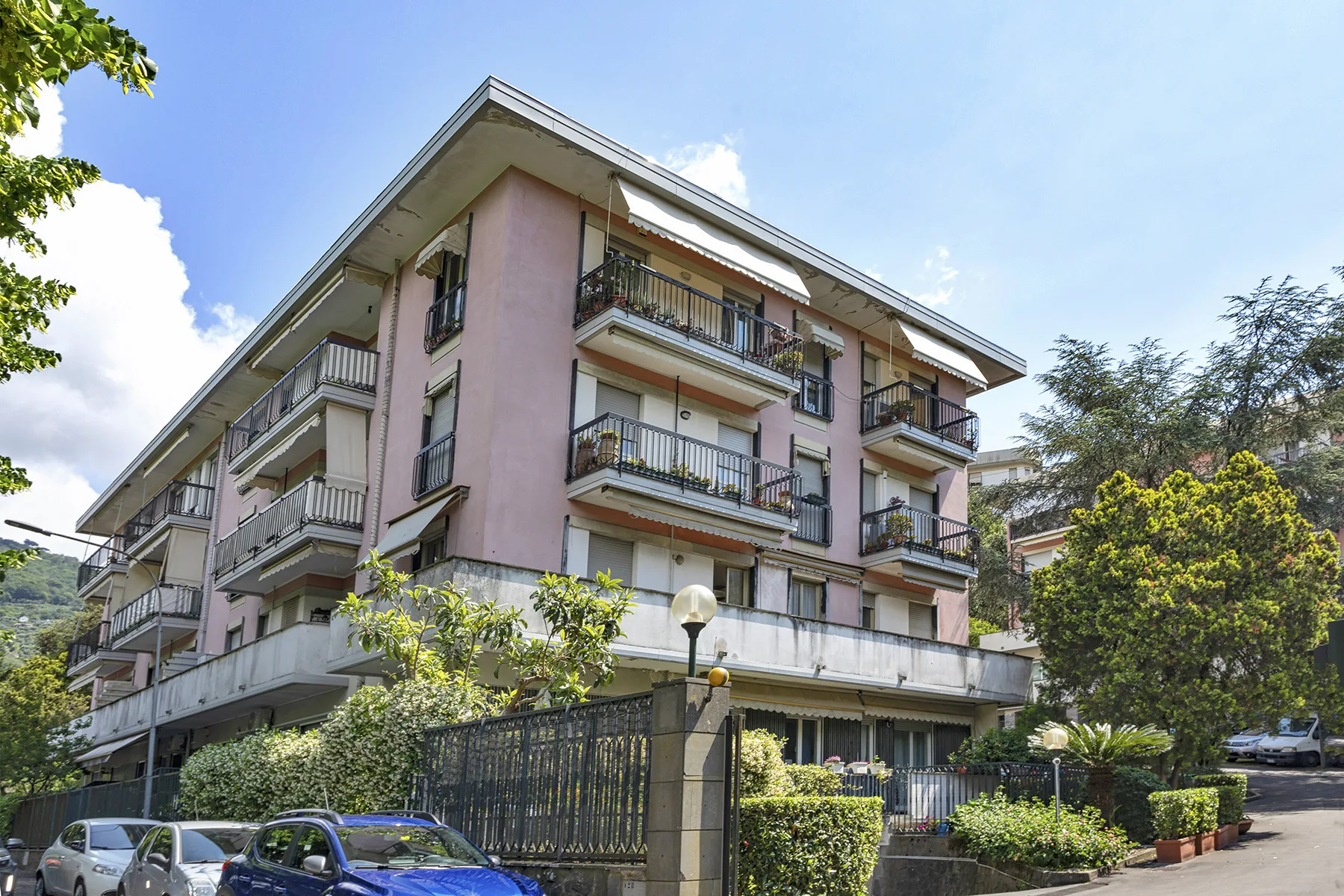Un edificio residencial de varias plantas con balcones se alza tras una entrada cerrada con reja.