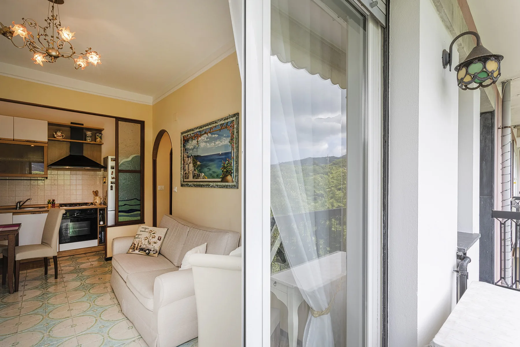 Una sala junto a una cocina abierta, con un sofá blanco y puertas de cristal.