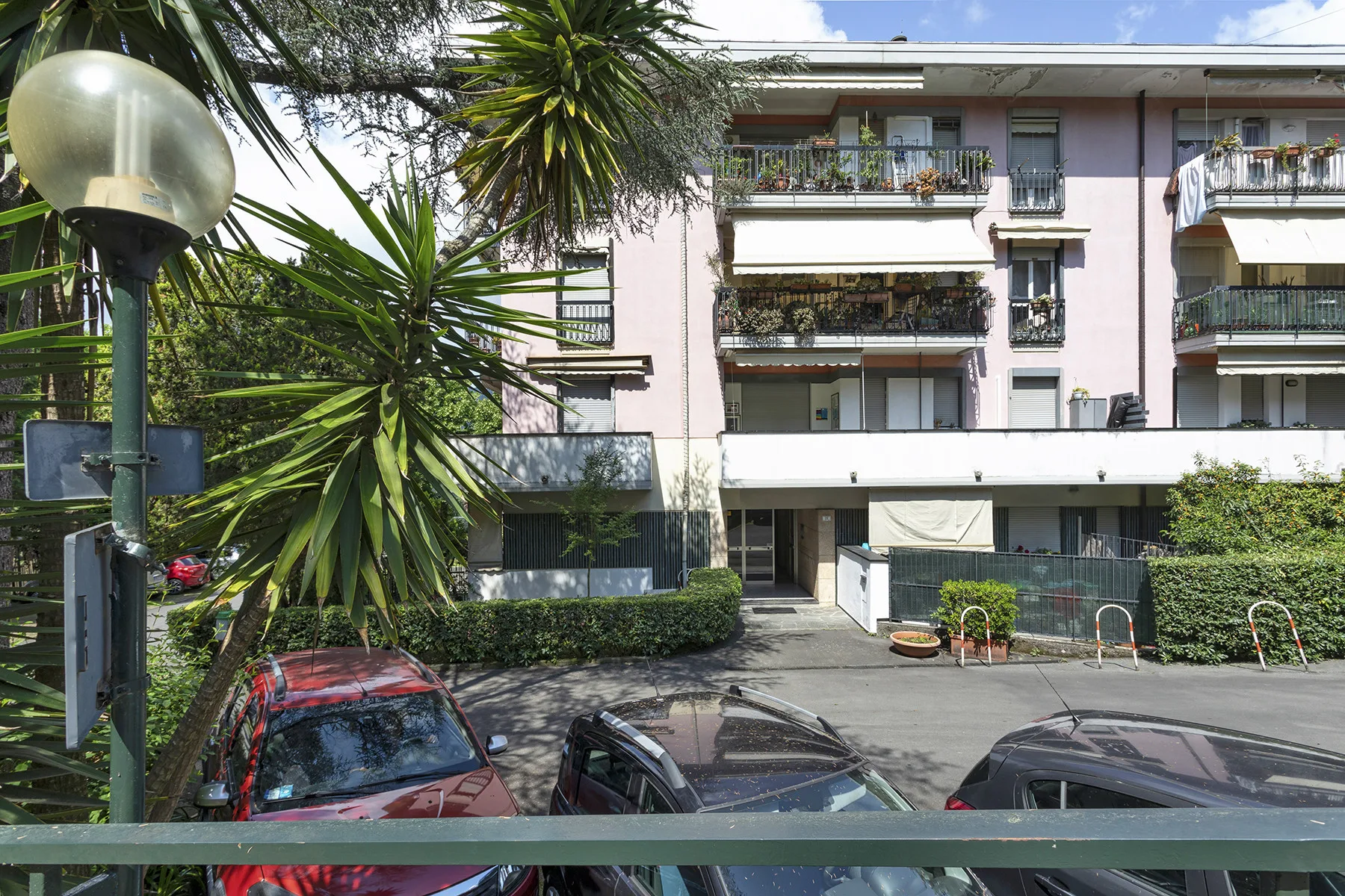 Un edificio de apartamentos rosa con balcones se alza detrás de una zona de estacionamiento pavimentada.