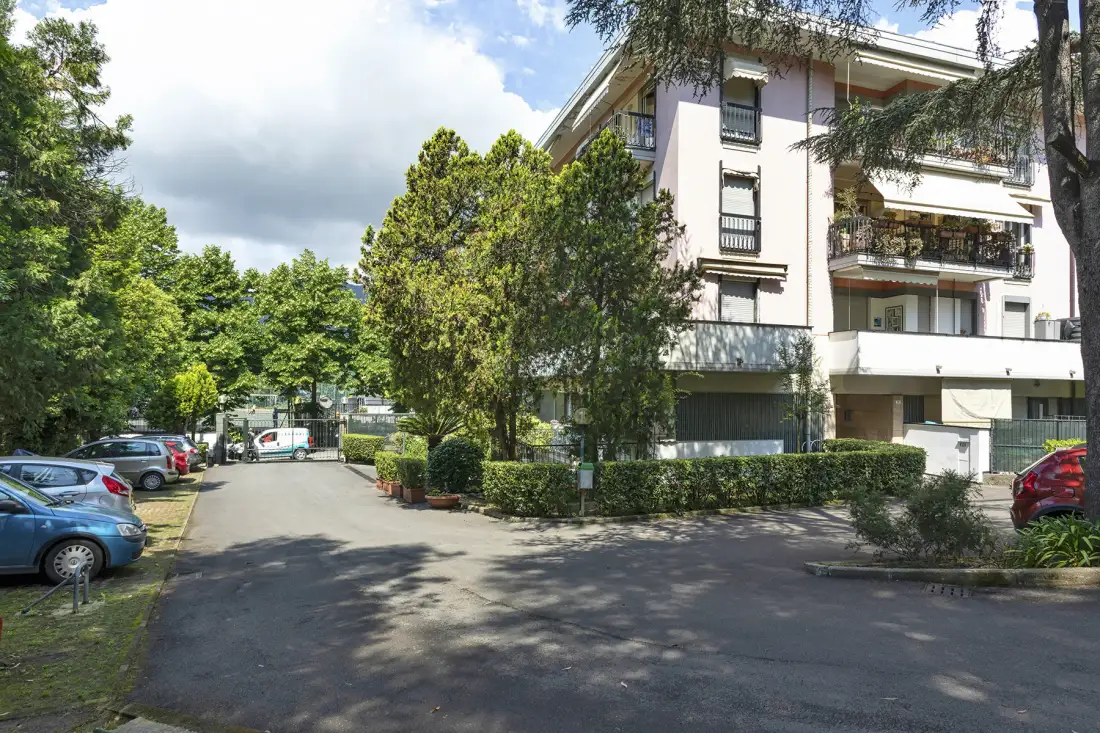 Un edificio de varias plantas se encuentra junto a una zona de estacionamiento arbolada.