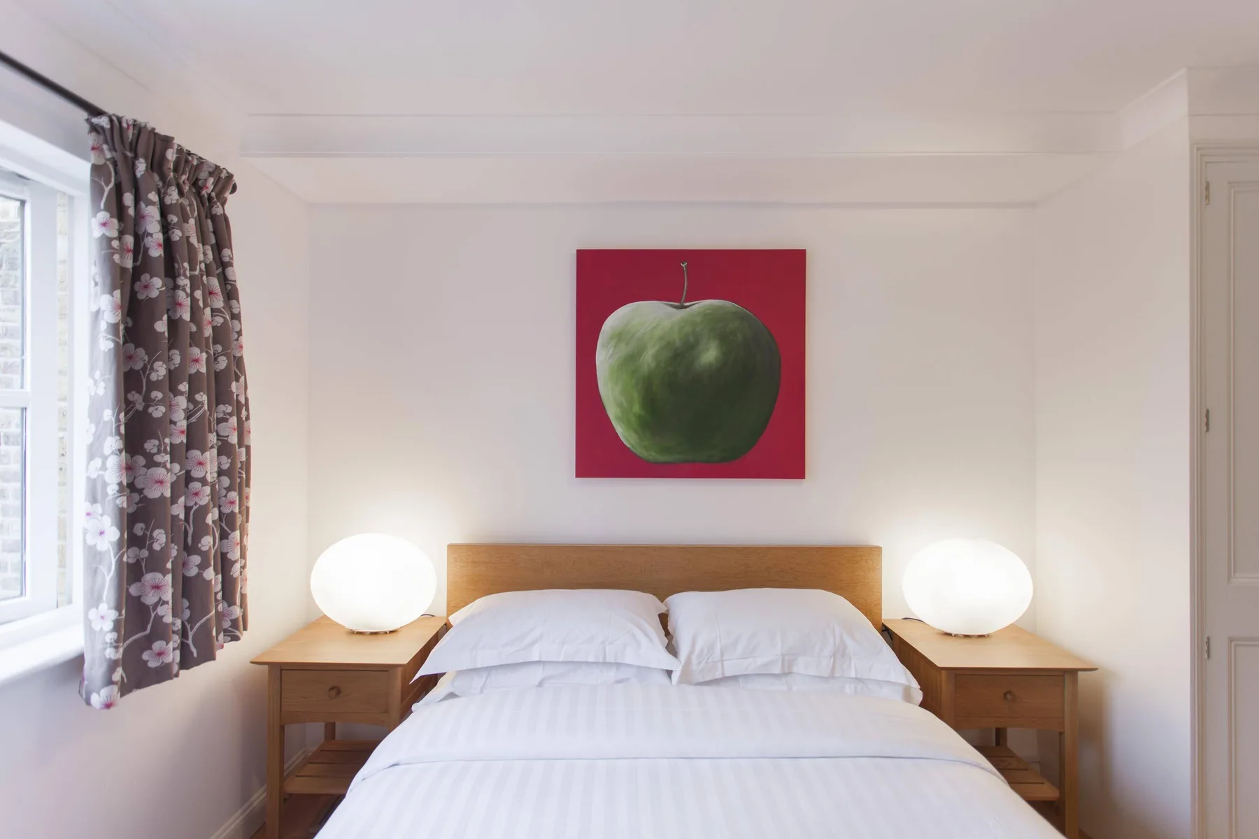 Un dormitorio con una cama bien arreglada bajo una pintura de una manzana verde.