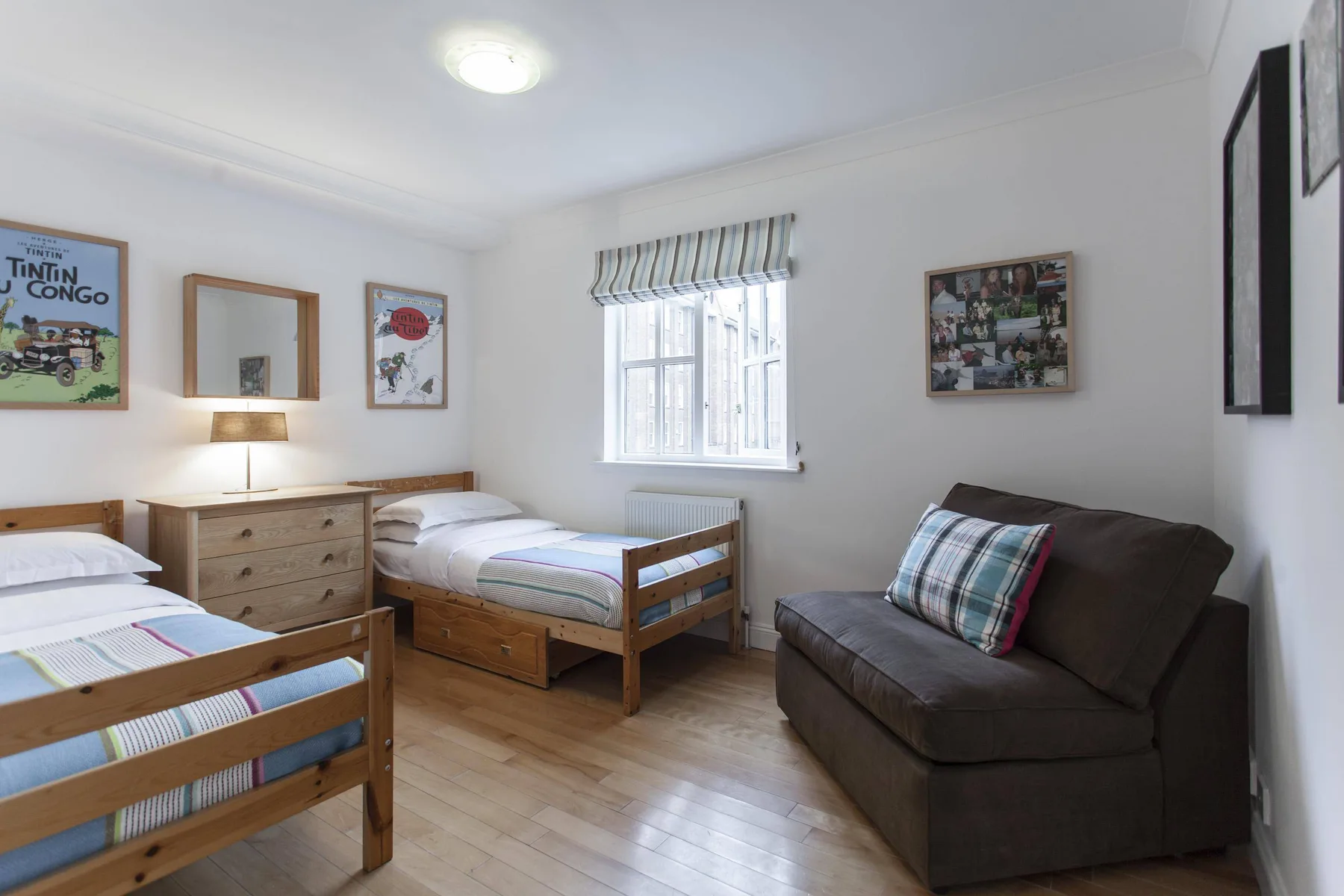 Un dormitorio luminoso con dos camas de madera, una cómoda y un sofá oscuro.