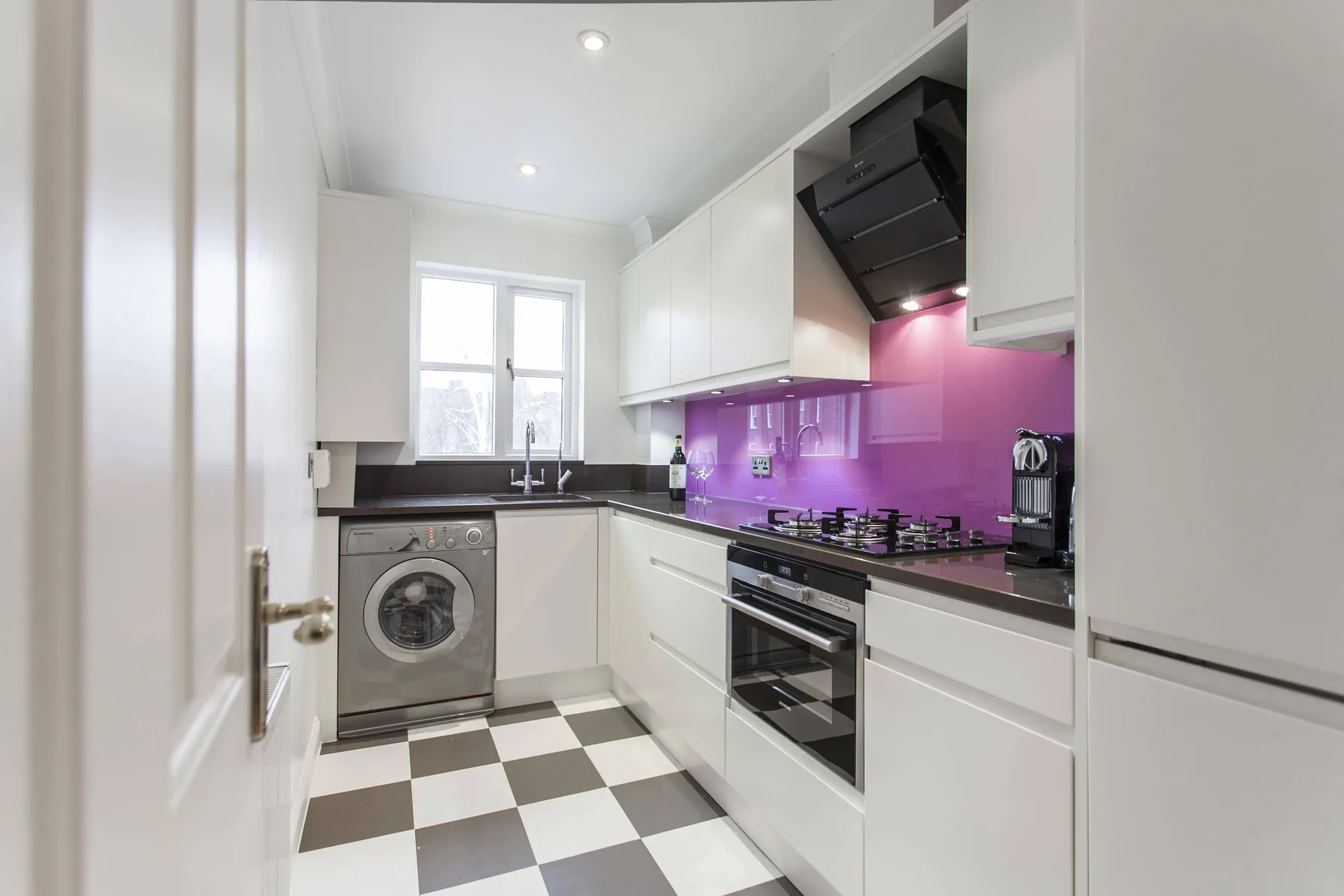 Una cocina luminosa y moderna con armarios blancos y suelo de cuadros blancos y negros.