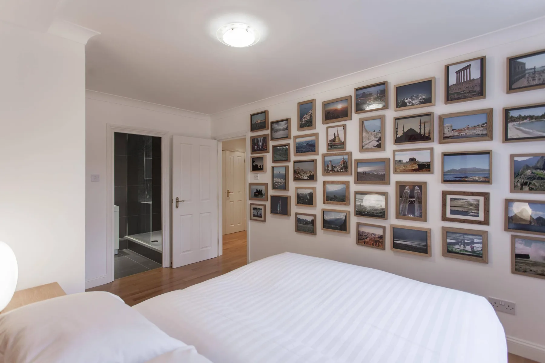 Un dormitorio con una cama blanca y una pared decorada con fotografías de paisajes enmarcadas.