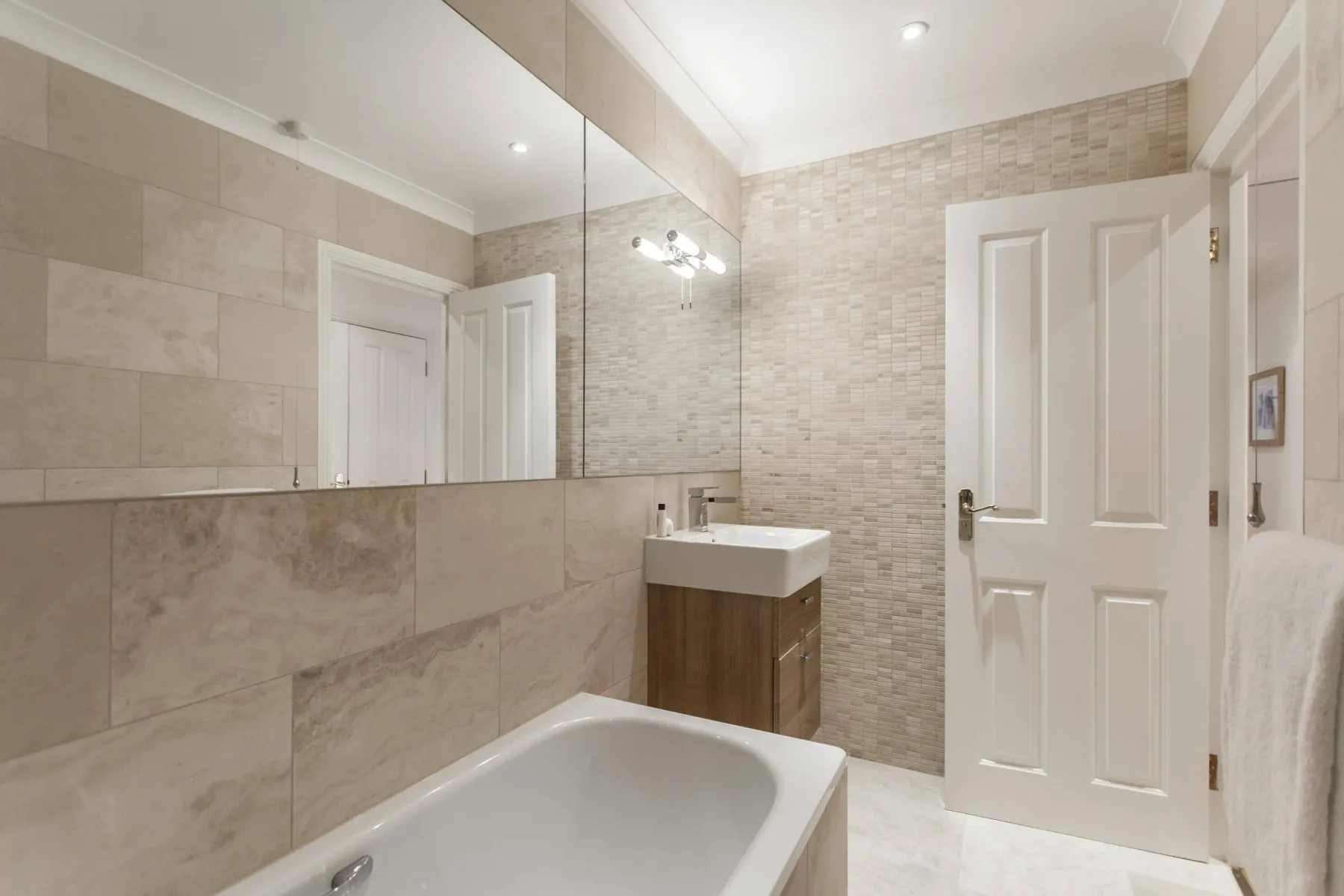 Baño revestido de azulejos con bañera, lavabo y un gran espejo.