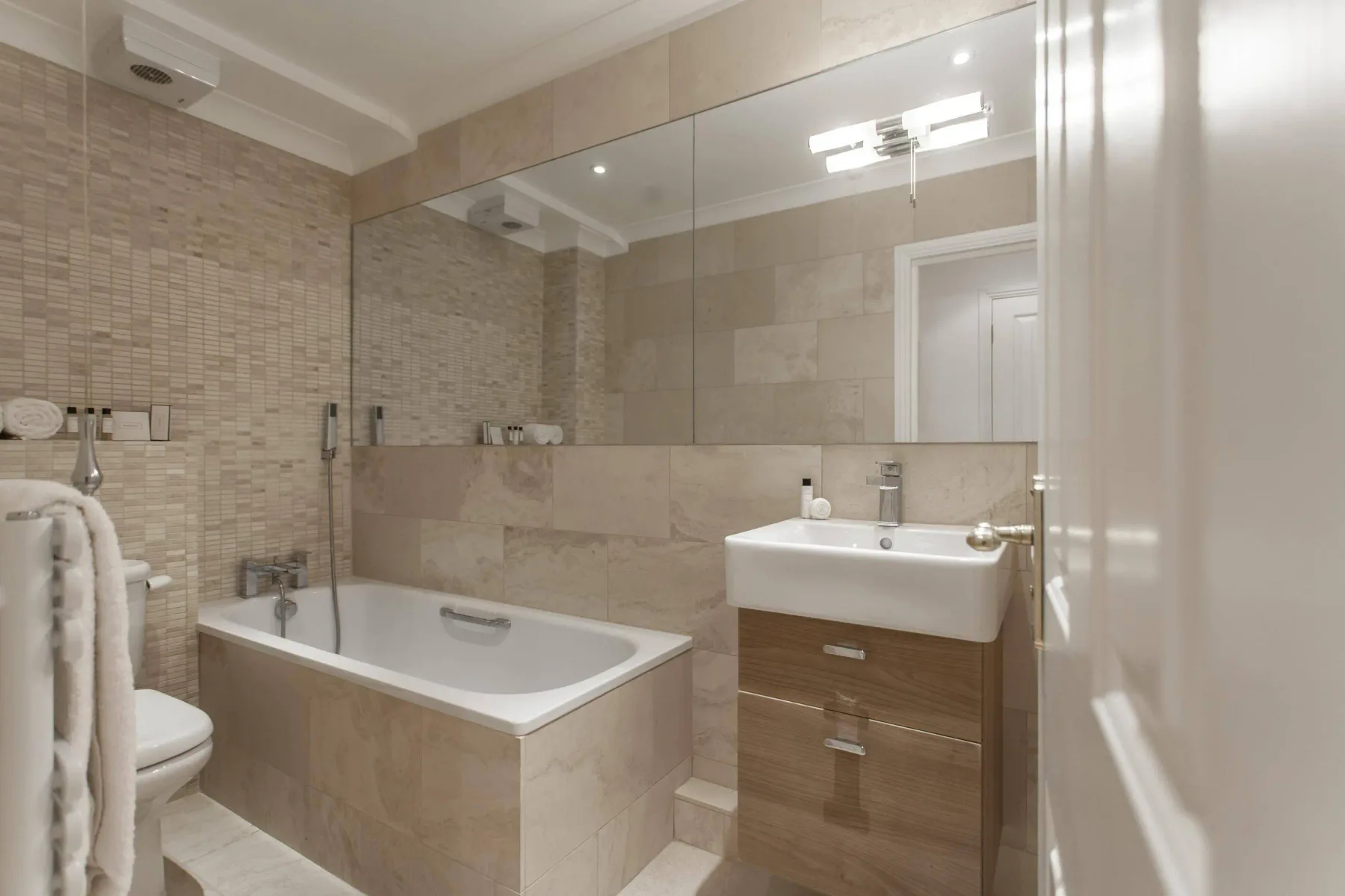 Baño alicatado con bañera, lavabo y un gran espejo en la pared.