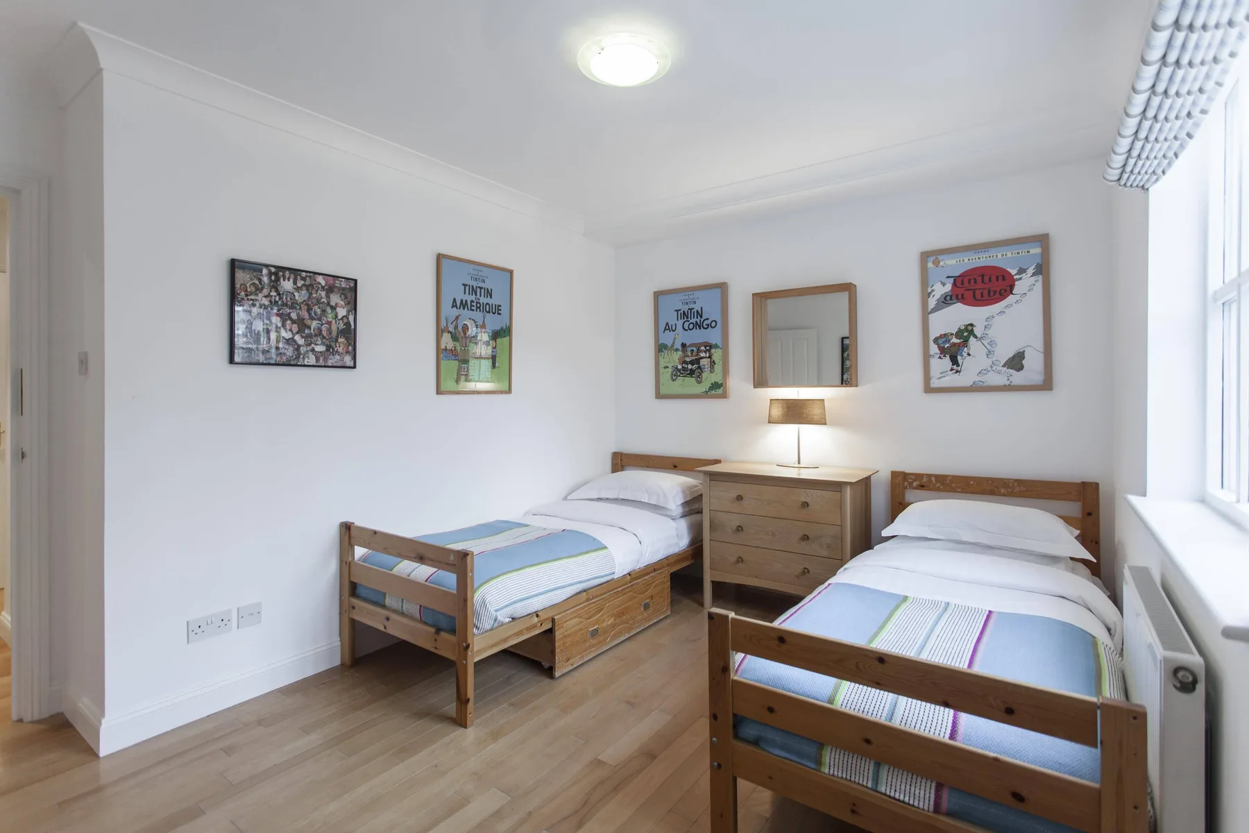 Un dormitorio luminoso con dos camas de madera y una cómoda.
