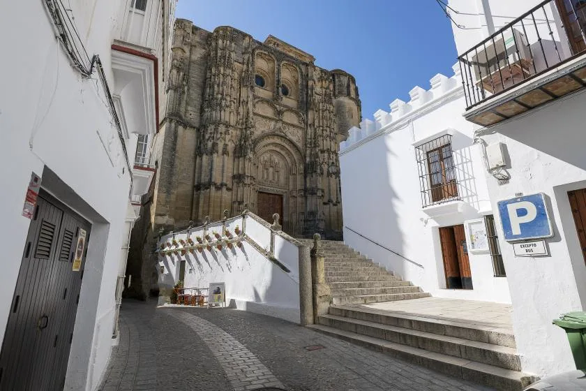 A narrow cobbled street leads to an ornate stone church entrance between white buildings.