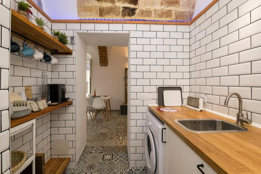 A narrow tiled kitchen with wooden countertops, a sink, and an open doorway.