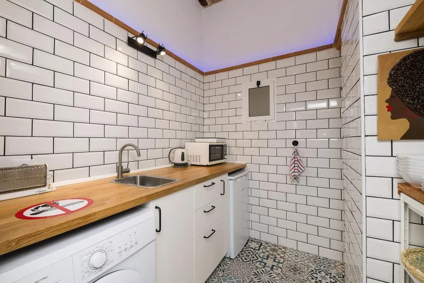 A compact kitchen with a wooden countertop, white cabinetry, and tiled walls.