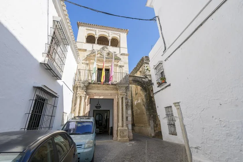 A narrow street opens onto an ornate stone building beneath a clear blue sky.
