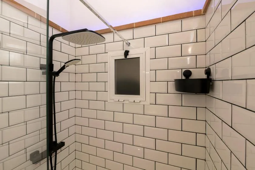 A tiled shower area with a large overhead showerhead and a small wall window.