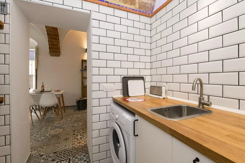 A compact kitchen with a sink and wooden countertop beside a tiled wall.