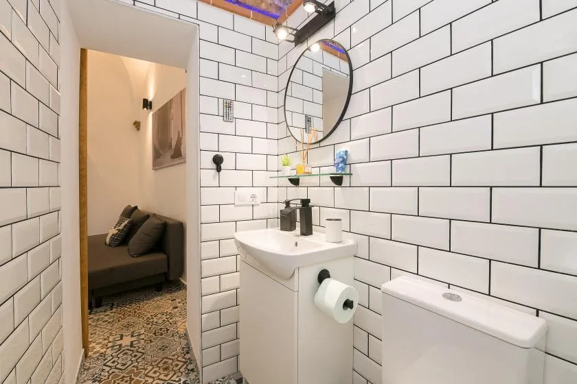 A tiled bathroom with a sink and mirror, opening onto a seating area.