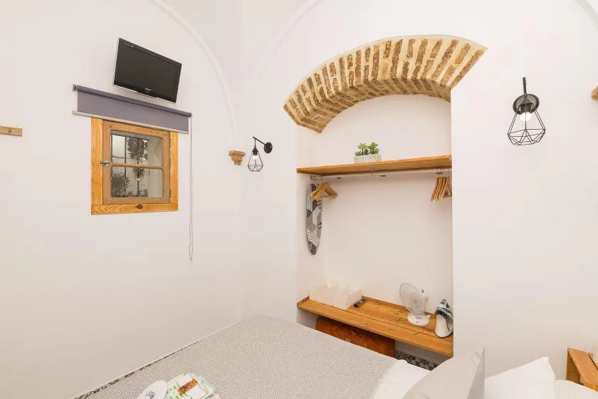 A bedroom with a bed, a wooden wall shelf, and a small window.