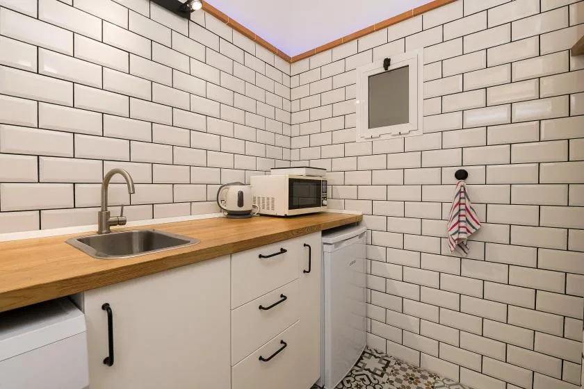 A compact kitchen with a wooden counter, sink, and white tiled walls.