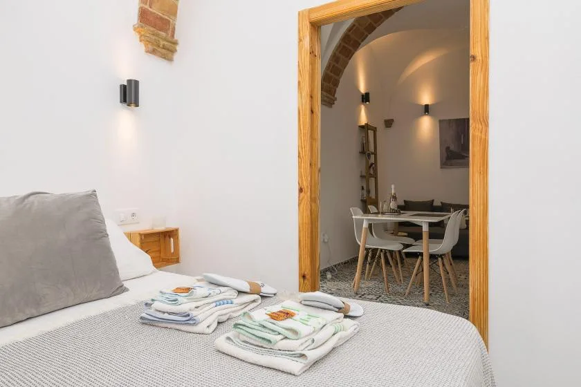 A bedroom with folded towels on the bed and a dining area visible through the doorway.