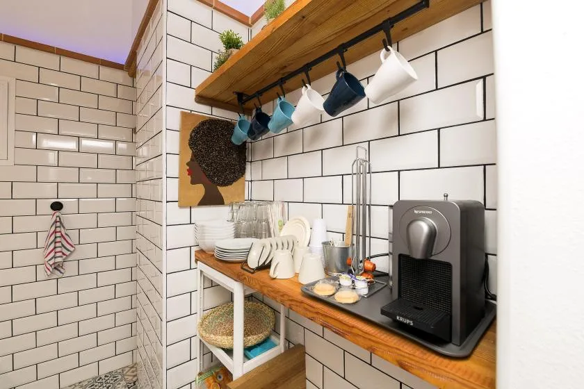 A compact coffee station with a machine and cups sits against white tiled walls.