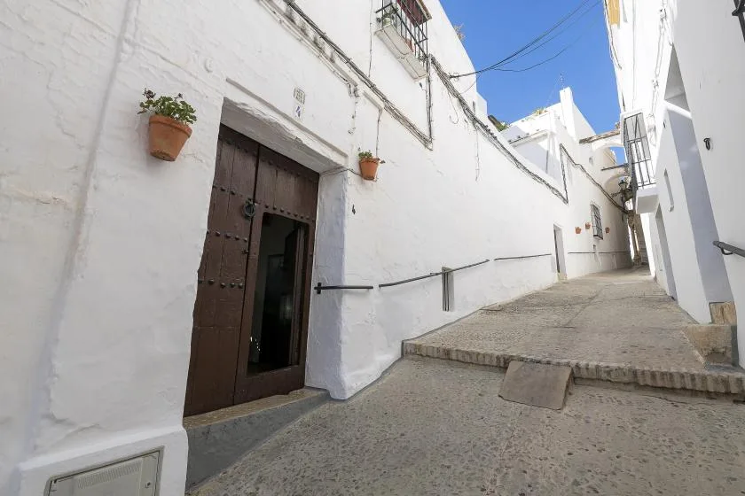A narrow paved alley runs between whitewashed buildings under a clear blue sky.