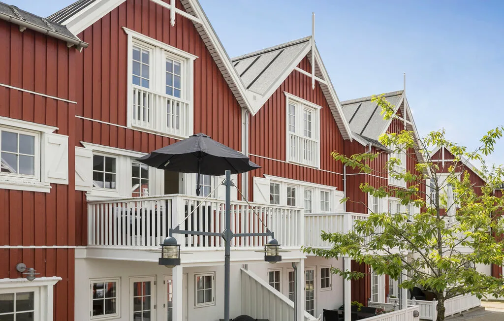 Casas adosadas de revestimiento rojo y balcones blancos bordean un paseo al aire libre.
