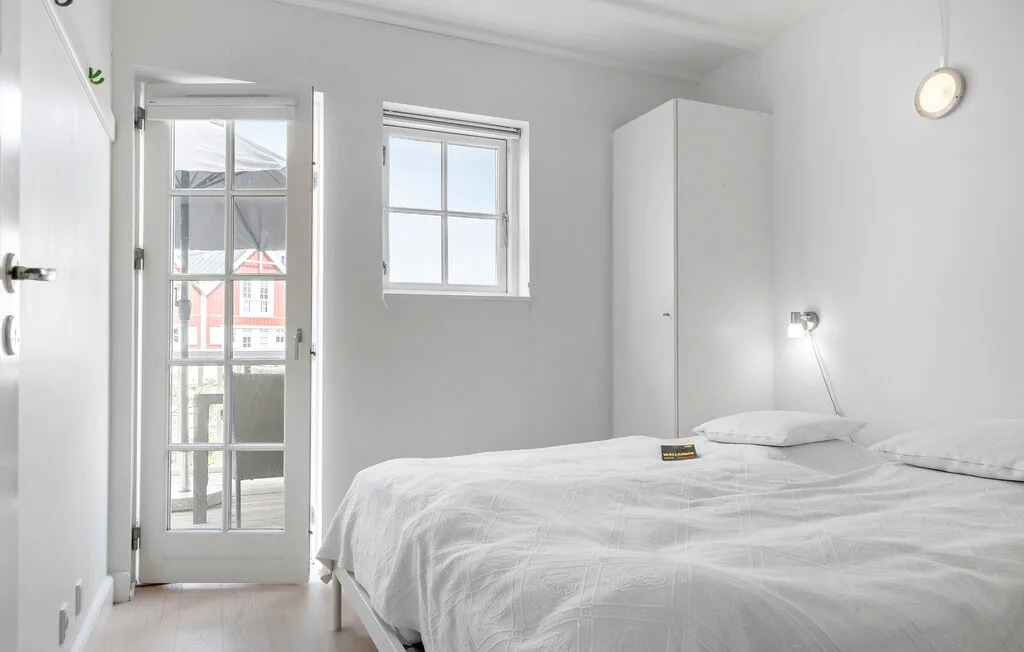Un dormitorio luminoso con ropa de cama blanca, una ventana y una puerta acristalada.