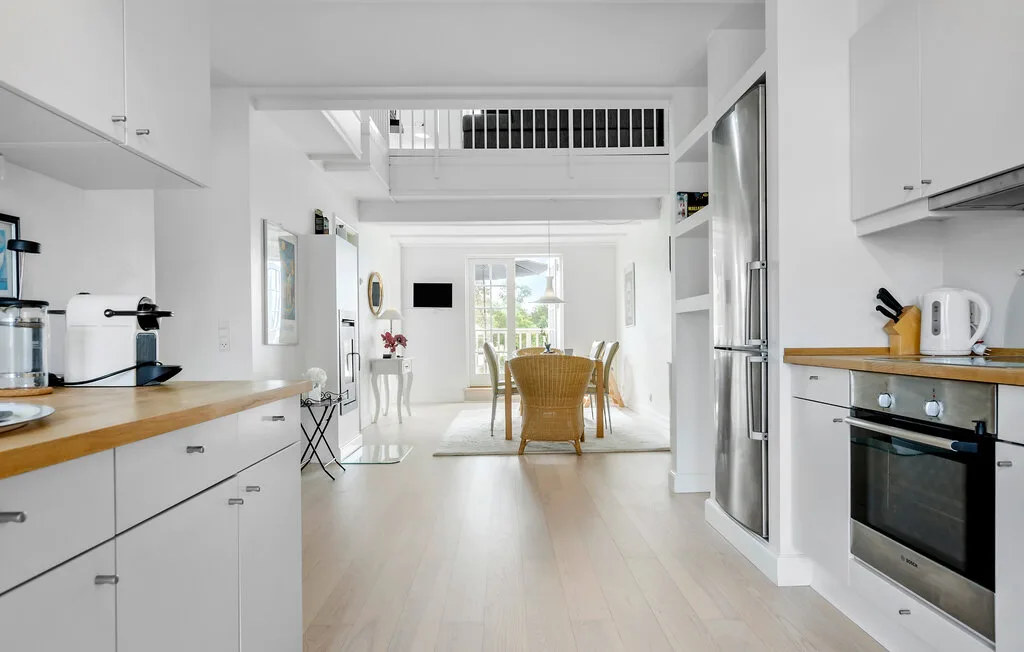 Cocina y comedor diáfanos y luminosos, con armarios blancos y una mesa de comedor.