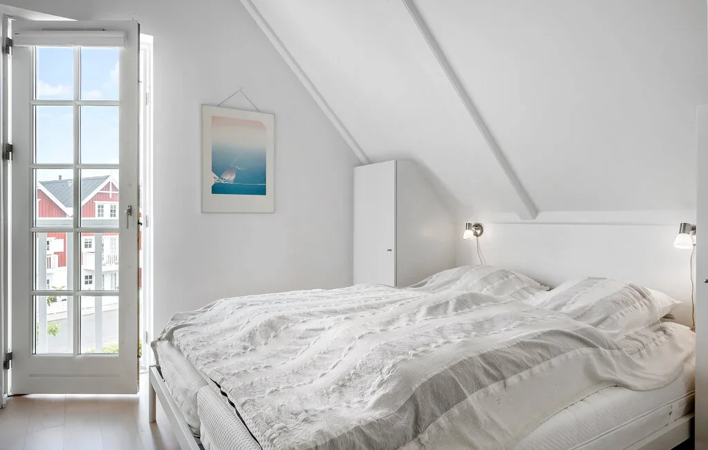 Un dormitorio con una cama bajo un techo inclinado y una ventana alta.