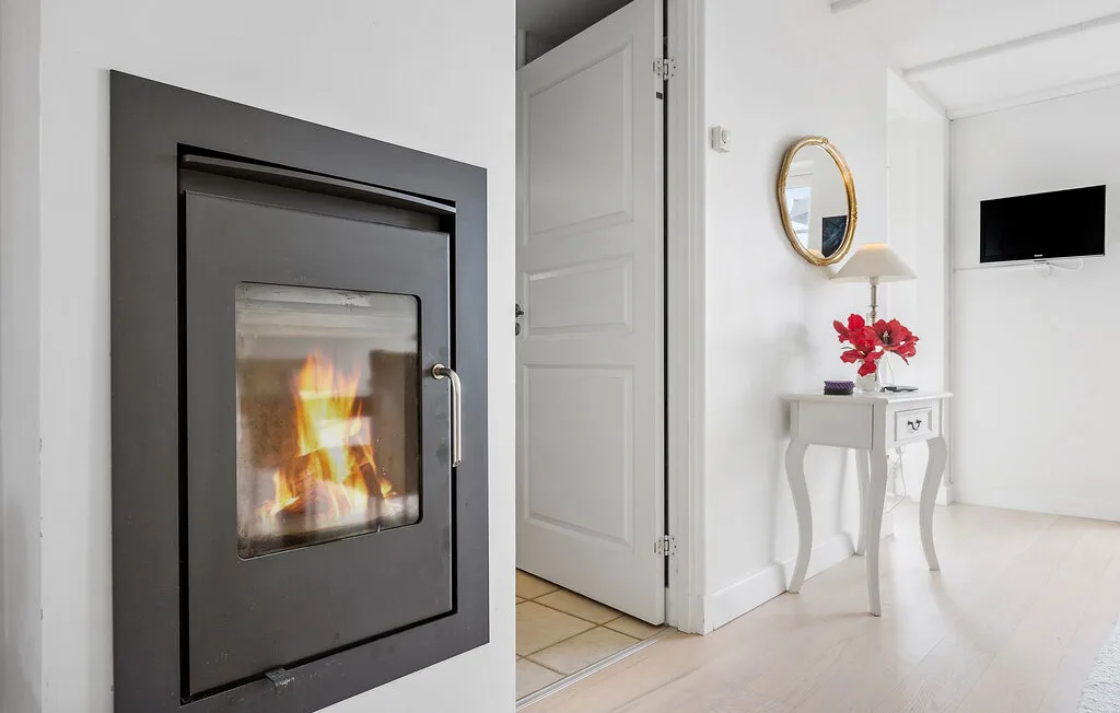 Una habitación luminosa con una chimenea de frente acristalado y una mesita con flores.