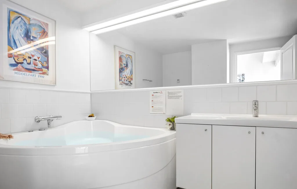 Un baño luminoso con una amplia bañera de esquina y paredes de azulejos blancos.