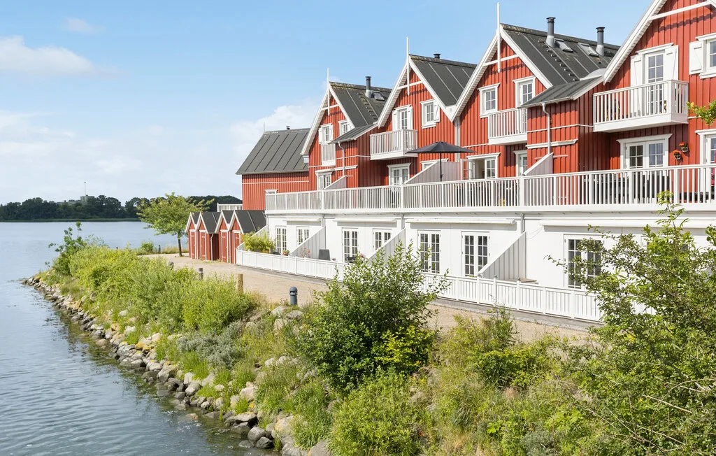Red waterfront buildings line a landscaped shore beside calm water.