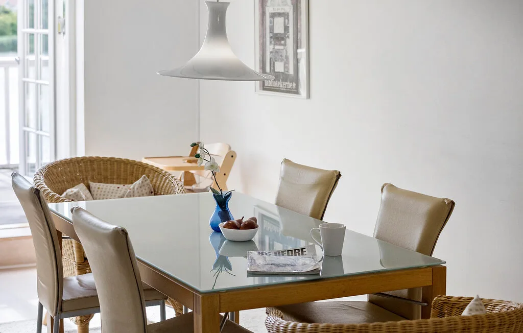 Un comedor luminoso cuenta con una mesa de vidrio y asientos tejidos.