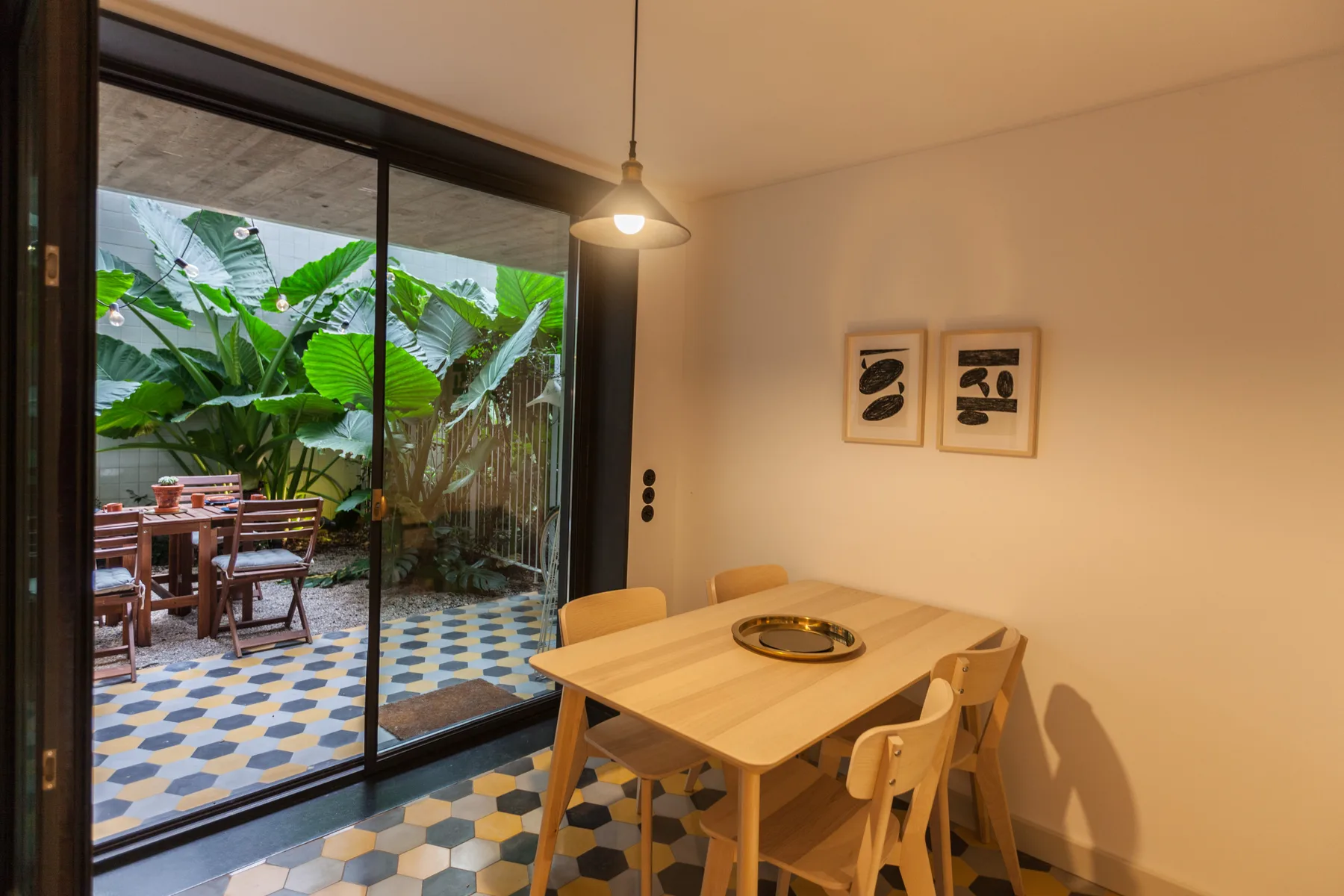 Un comedor se abre a un patio frondoso a través de grandes puertas corredizas de vidrio.