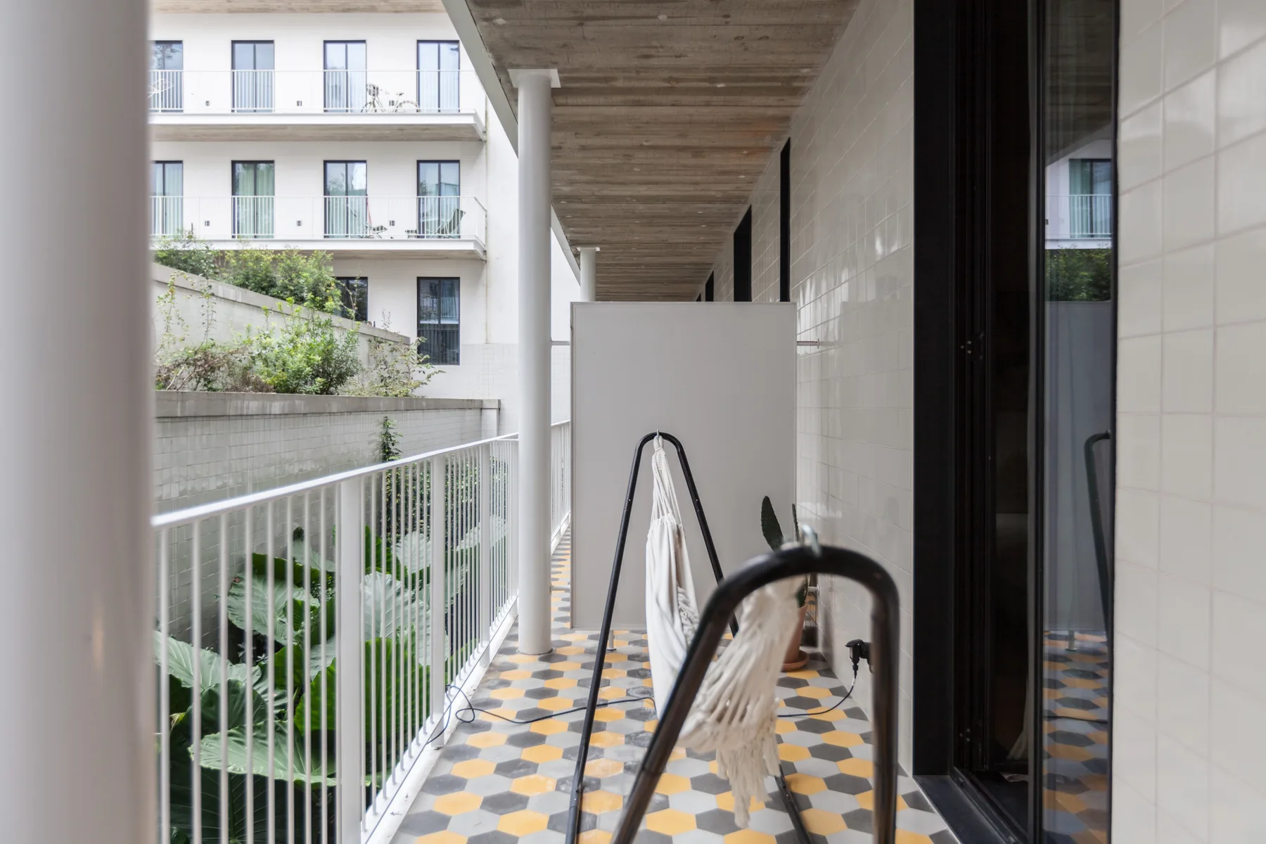 Un pasillo exterior de baldosas da a un patio frondoso junto a un edificio moderno.