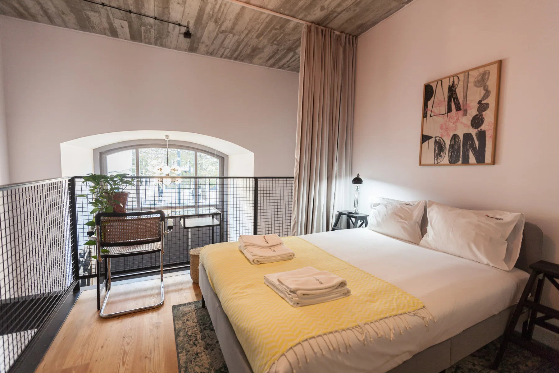 Un dormitorio con una cama junto a una ventana alta y una pequeña zona de estar.