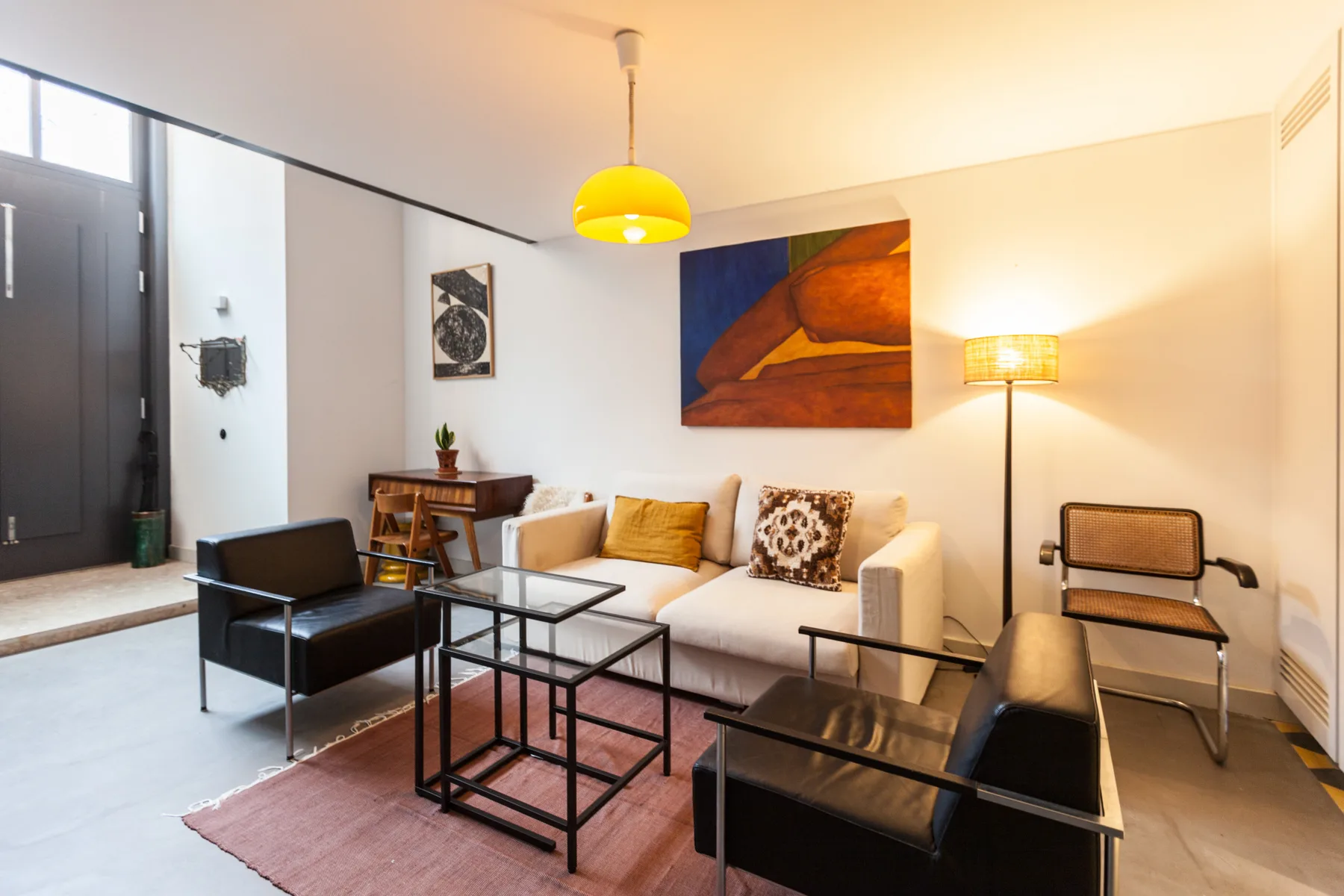 Una sala de estar con un sofá blanco, asientos oscuros y una mesa de centro de cristal.
