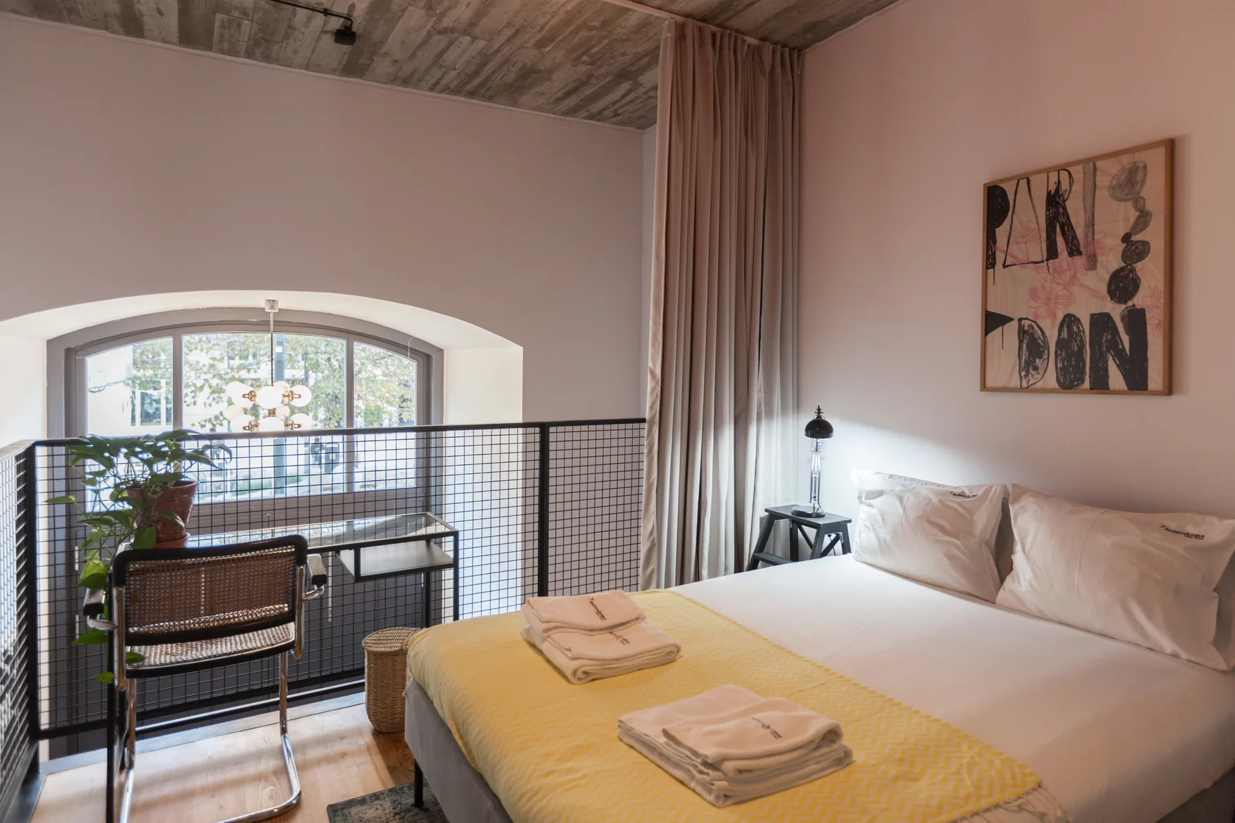 Dormitorio con una cama junto a una ventana con cortinas y una barandilla negra.