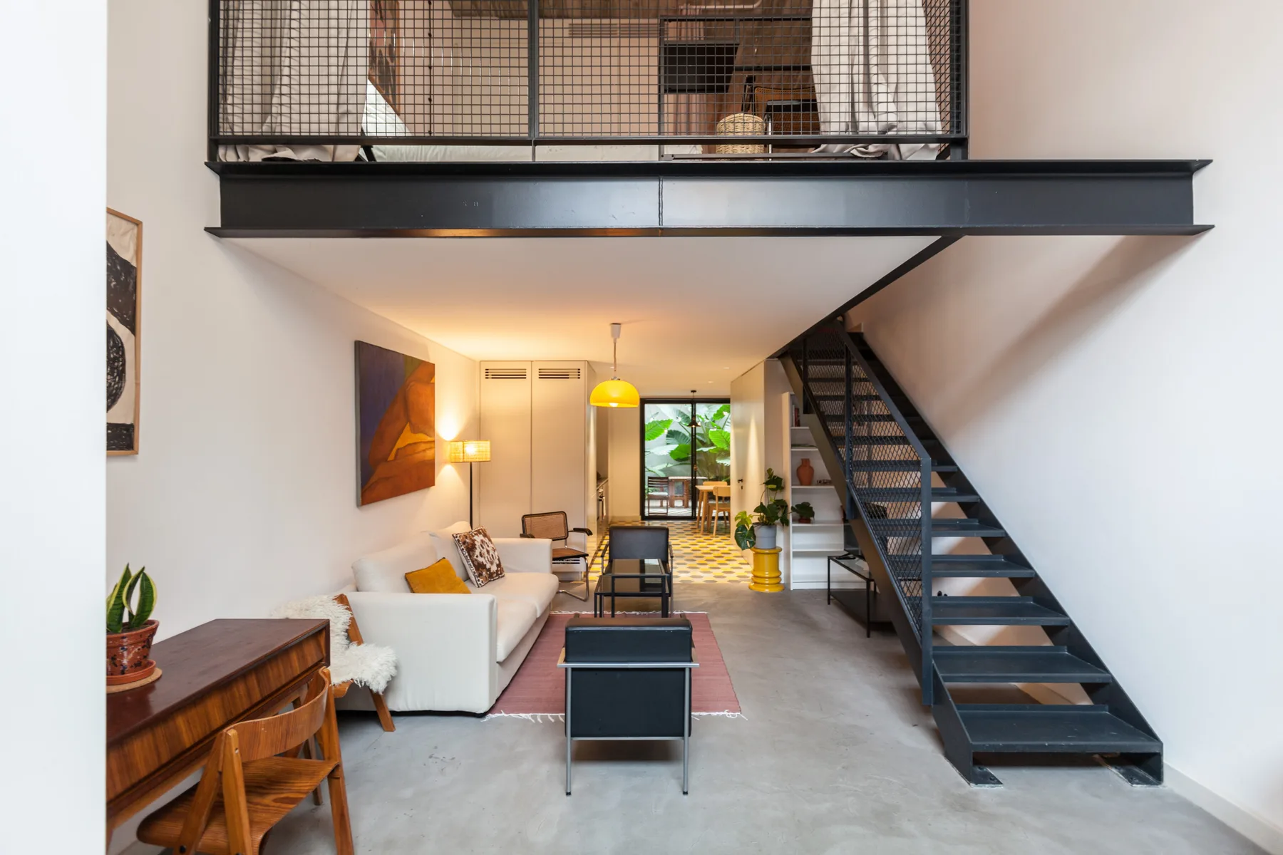 Una sala de estar luminosa con asientos y una escalera que lleva a un nivel superior.