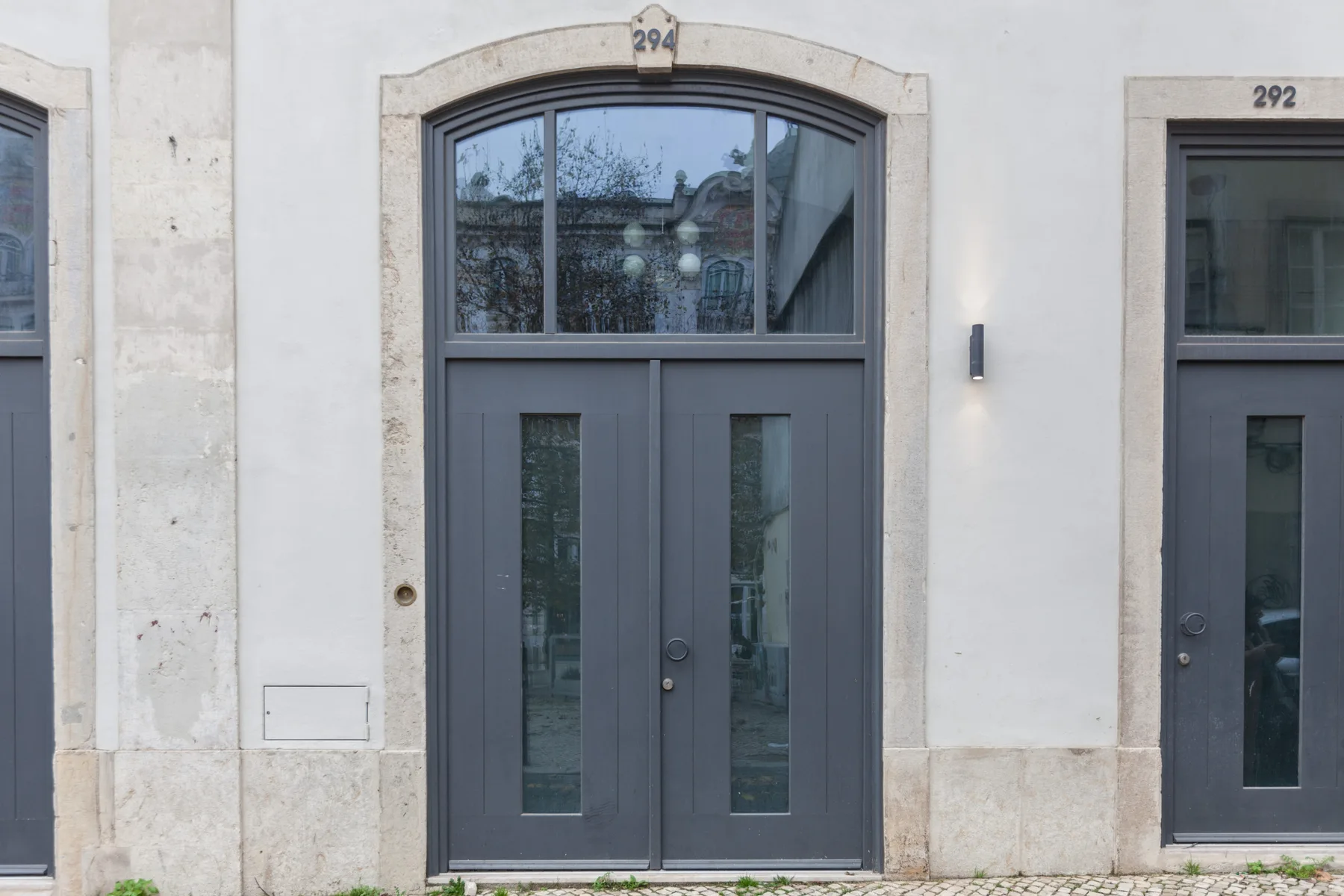 Una puerta gris con paneles de vidrio está en una fachada clara.