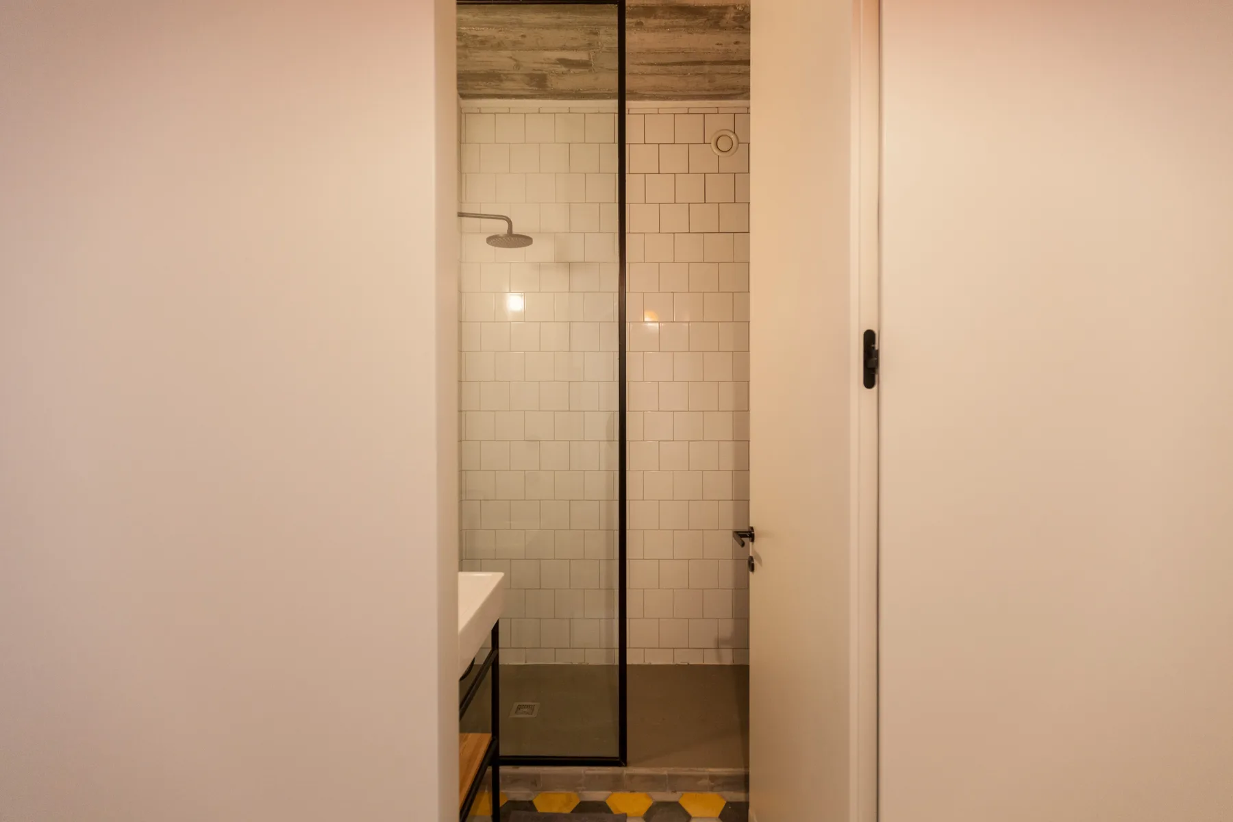 Baño con una mampara de vidrio y paredes de azulejos blancos.