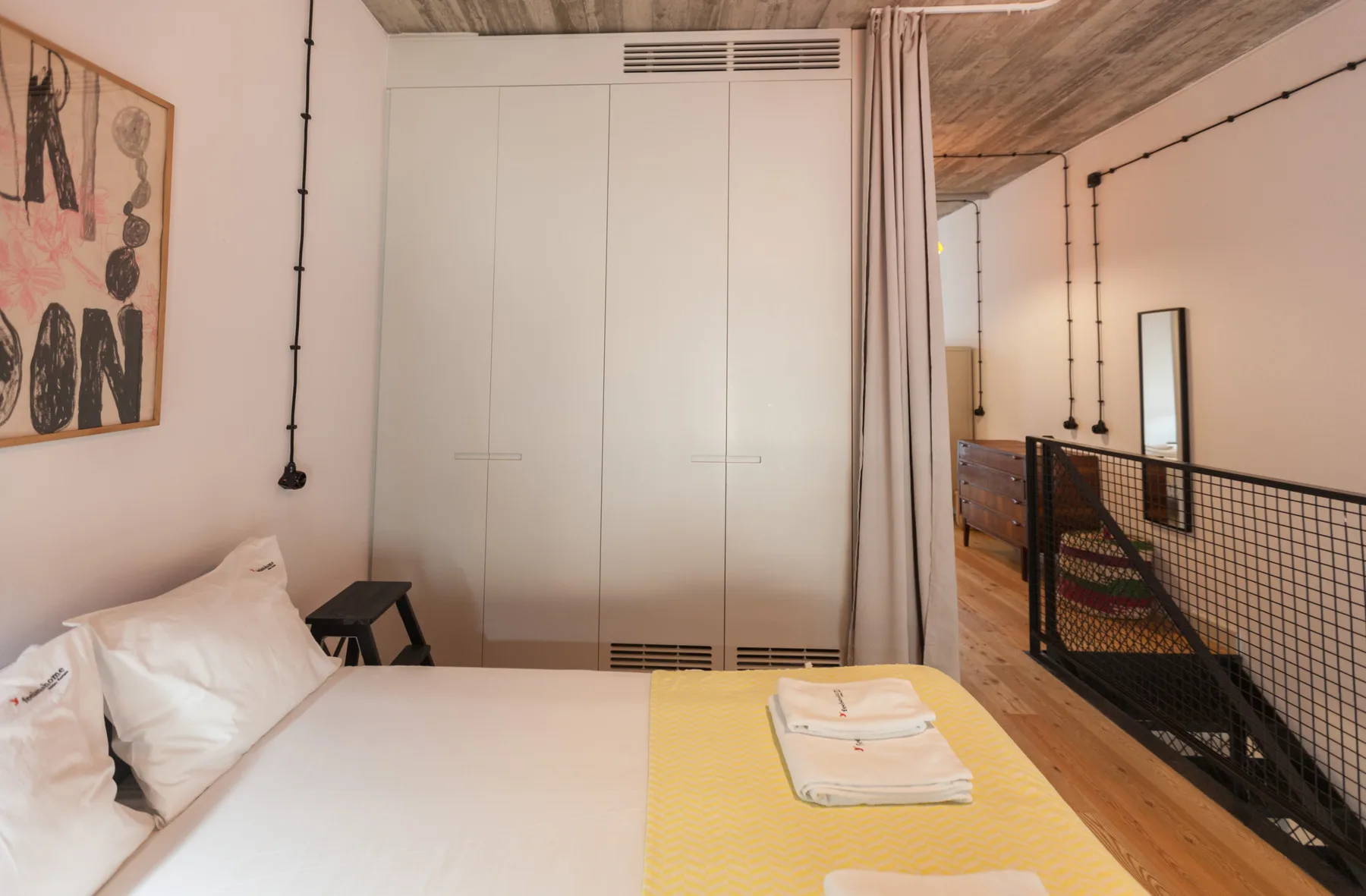 Un dormitorio con una cama junto a una barandilla de entreplanta con cortina.