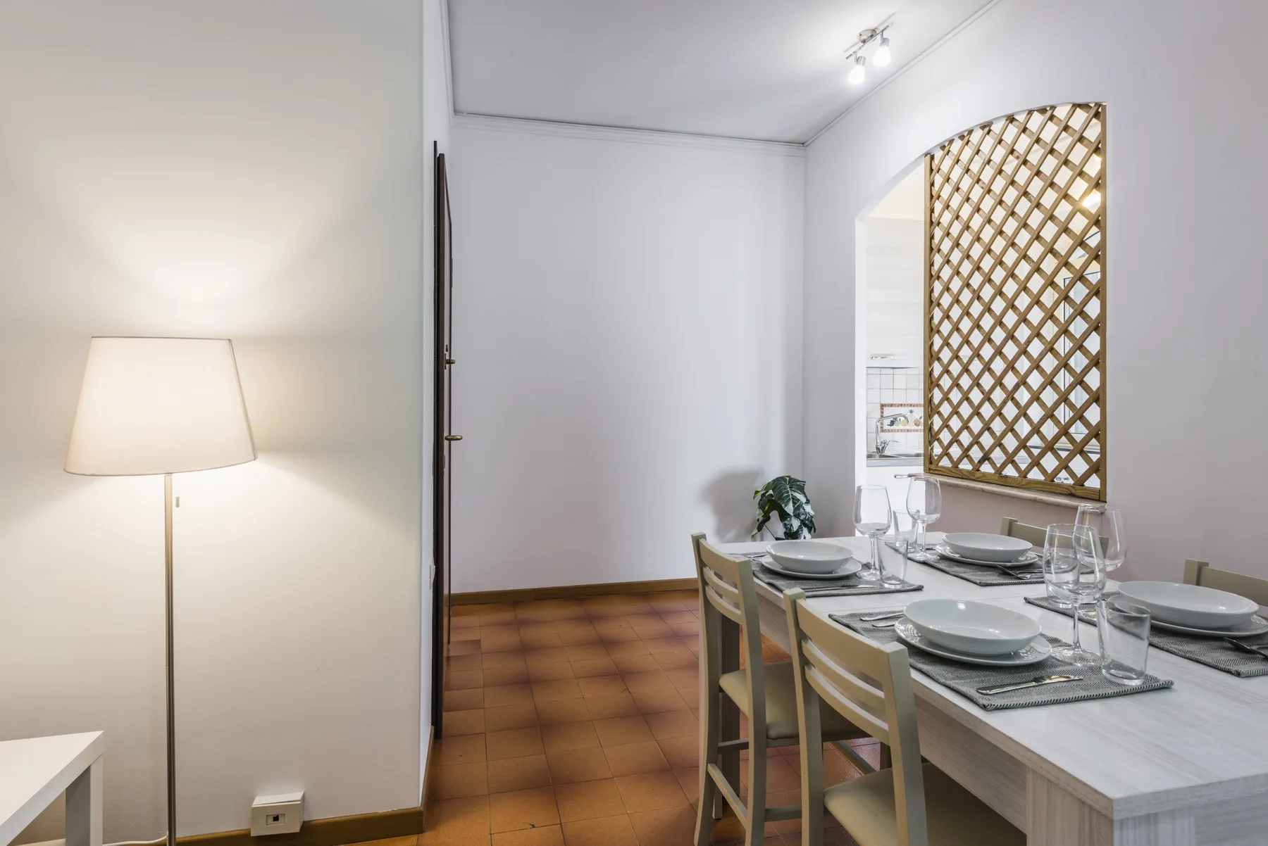 Un comedor con la mesa puesta junto a una pared blanca y una celosía.