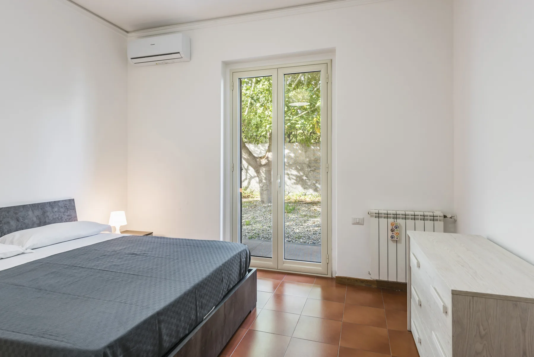 Un dormitorio con una cama junto a puertas de vidrio y una vista frondosa.