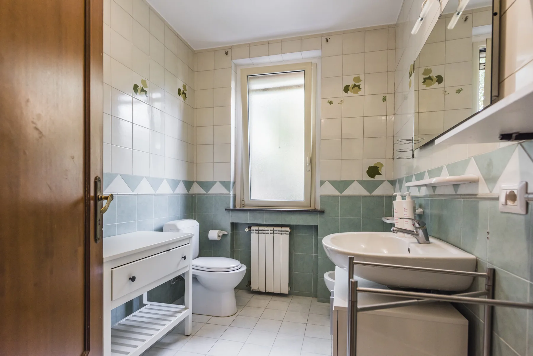 Un baño con azulejos, lavabo, inodoro y una ventana esmerilada.