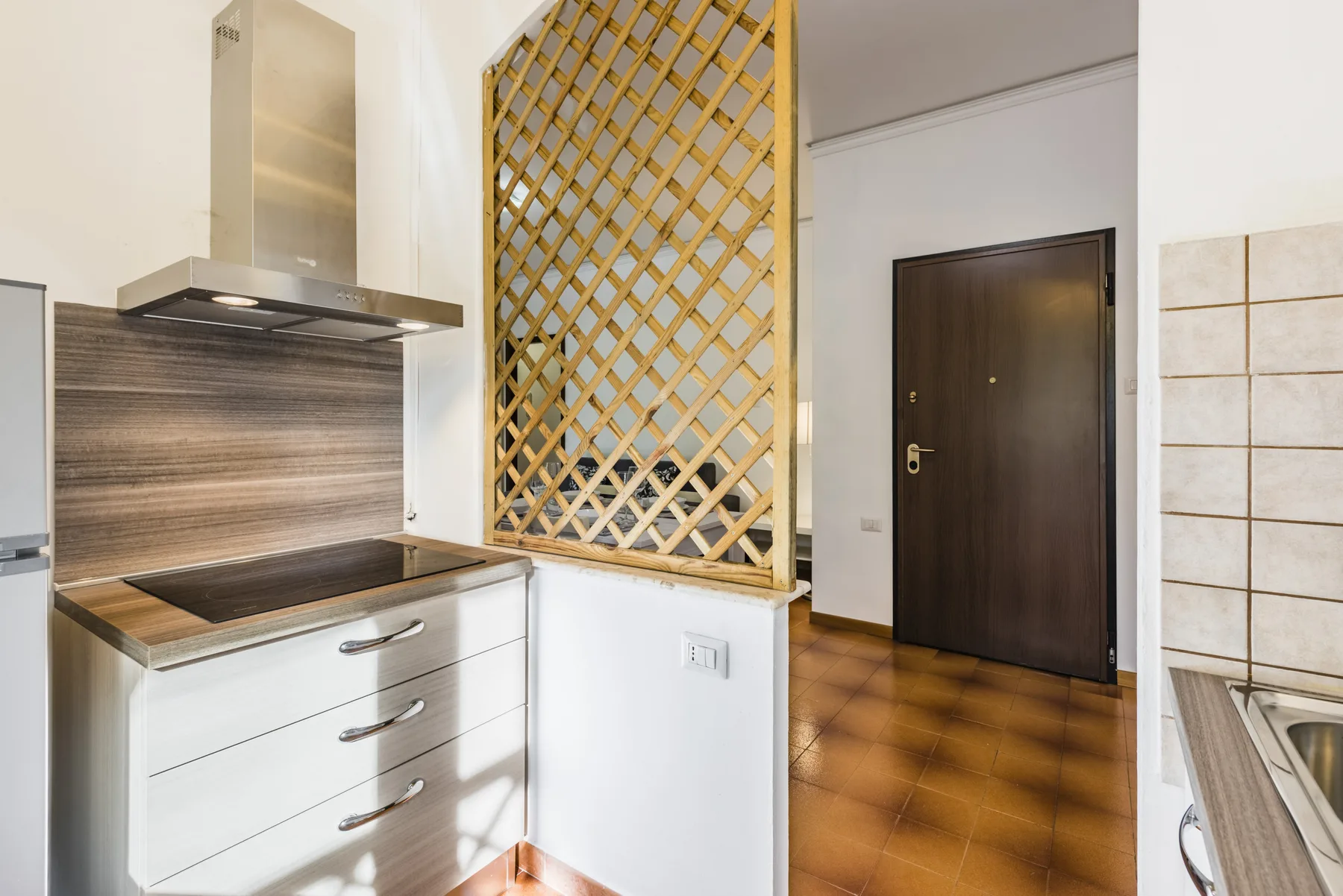 La zona de cocina se abre a una entrada con suelo de baldosas y una puerta oscura.
